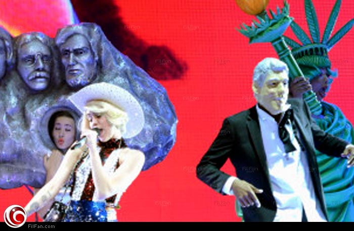 مايلي سايرس مع عضو فريقها المرتدي لقناع كلينتون